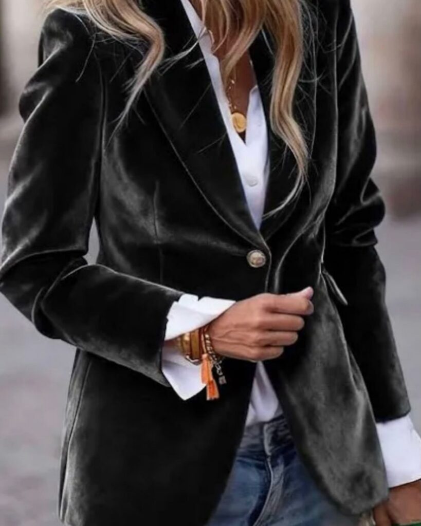 A person wearing a dark green velvet blazer over a white shirt and blue jeans.