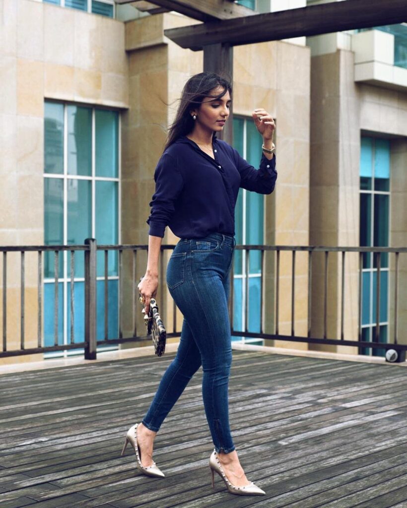 A woman walking across a wooden deck wearing a navy blouse and blue skinny jeans.