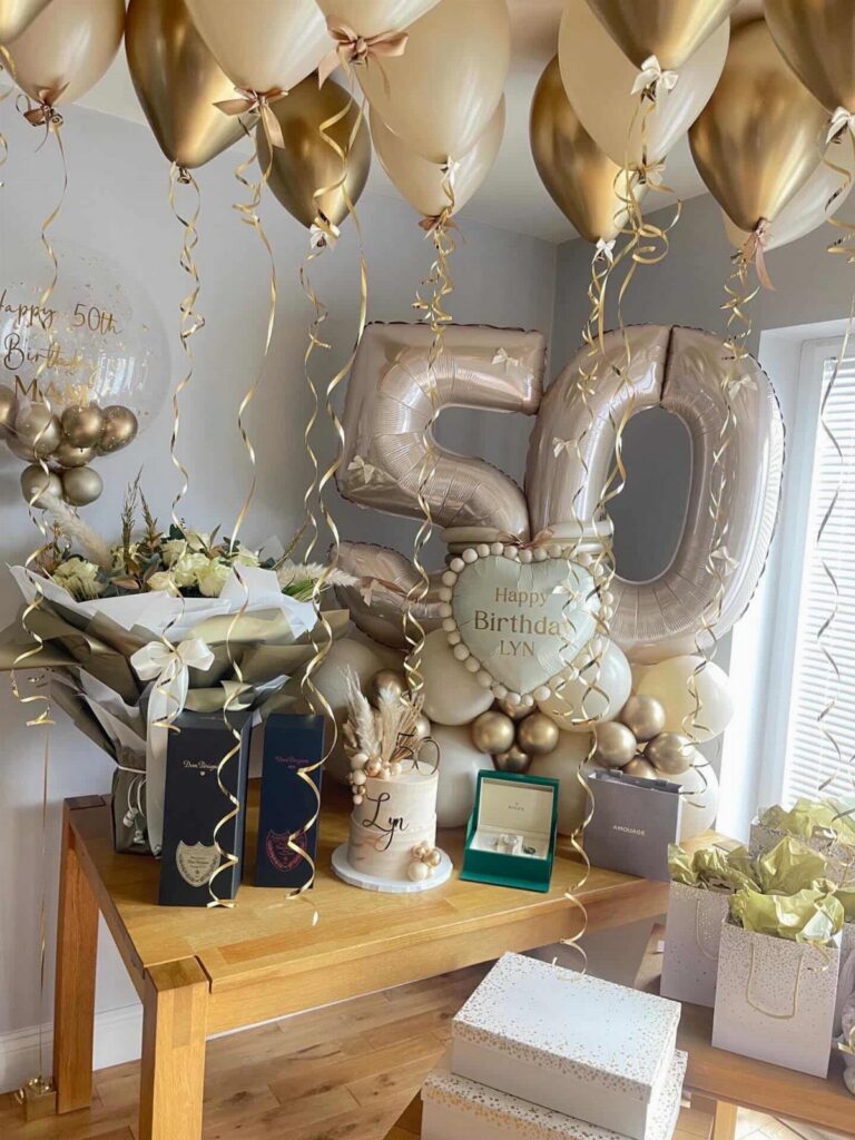 Gold and cream balloons surrounding large rose gold number fifty balloons and birthday gifts.