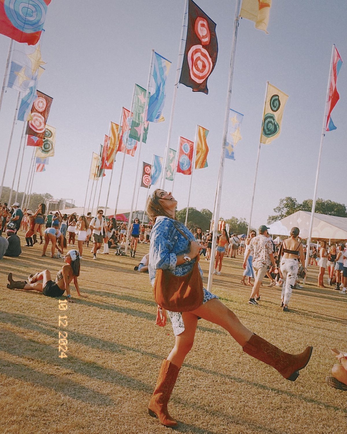Woman in a blue dress and brown cowboy boots posing in a field with colorful flags.