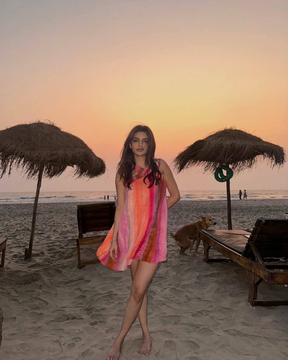 A woman in a colorful tie-dye tunic dress posing on a beach at sunset.