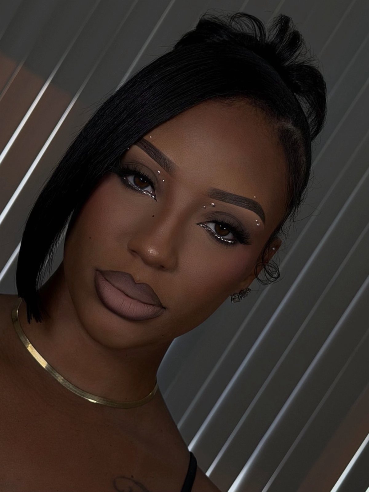 Woman with neutral makeup and a gold choker necklace looking towards the camera.