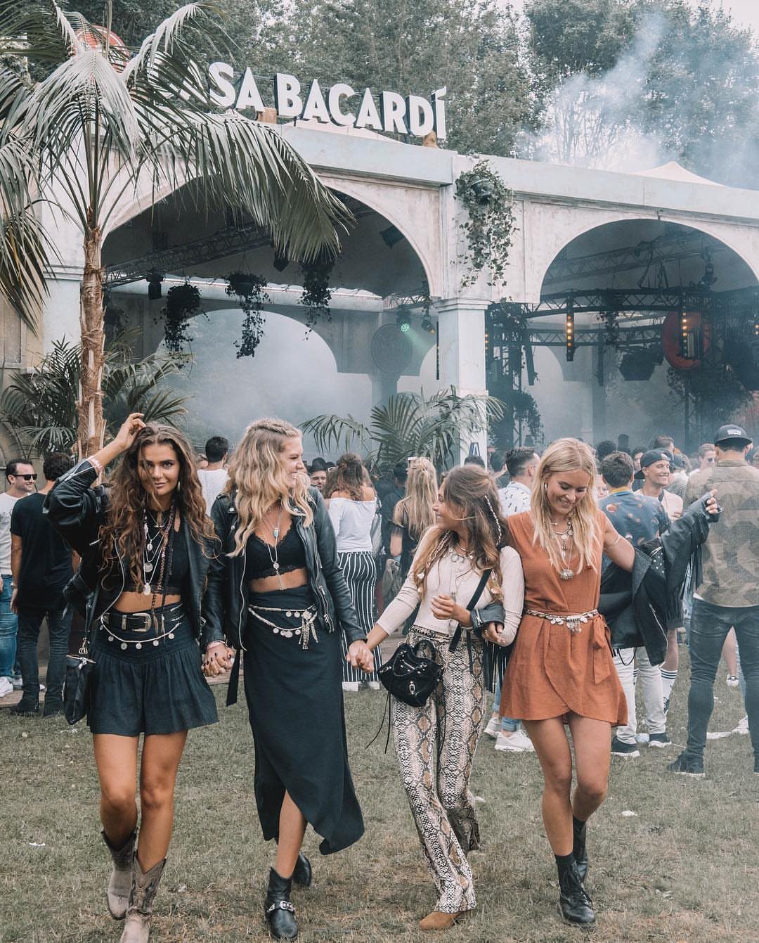 Four women walking through a music festival wearing bohemian style festival clothing.