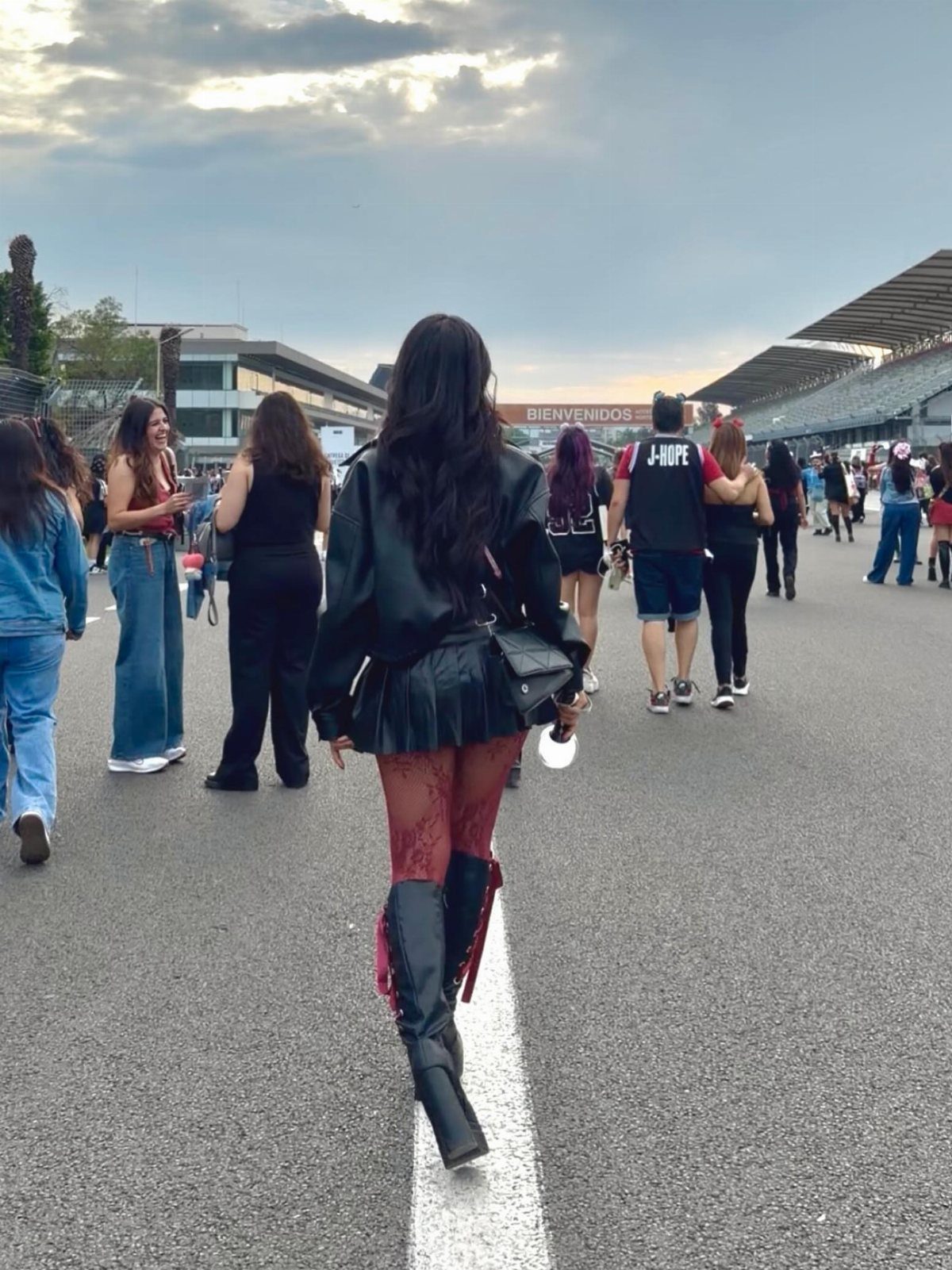Woman walking in a black leather jacket, skirt, red tights, and tall black boots.