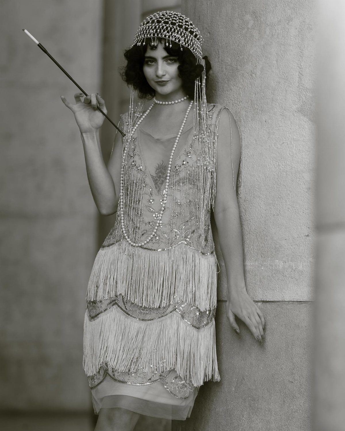 A woman wearing a beaded flapper costume and headband holding a long cigarette holder.