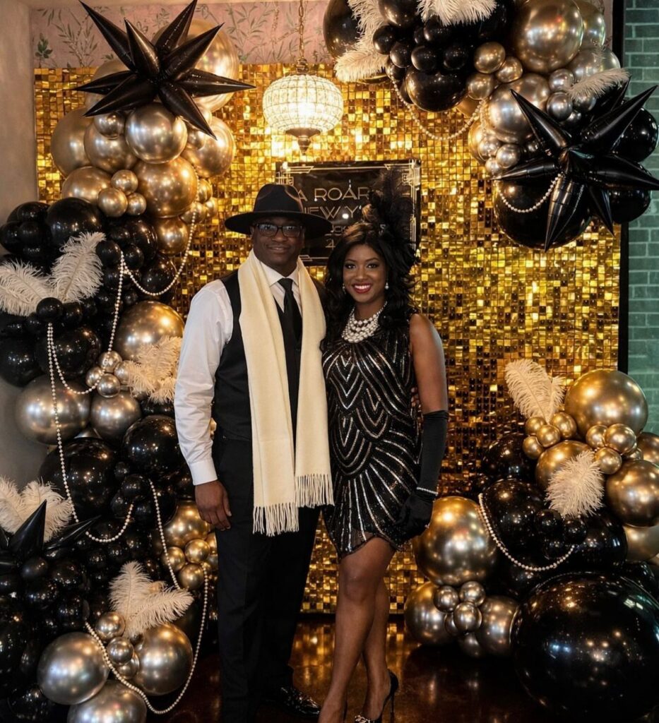 Man and woman in 1920s inspired attire posing against a gold sequin and balloon backdrop.