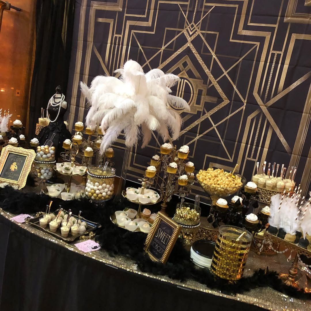 A dessert table with white feathers and gold geometric patterns for a Gatsby themed party.