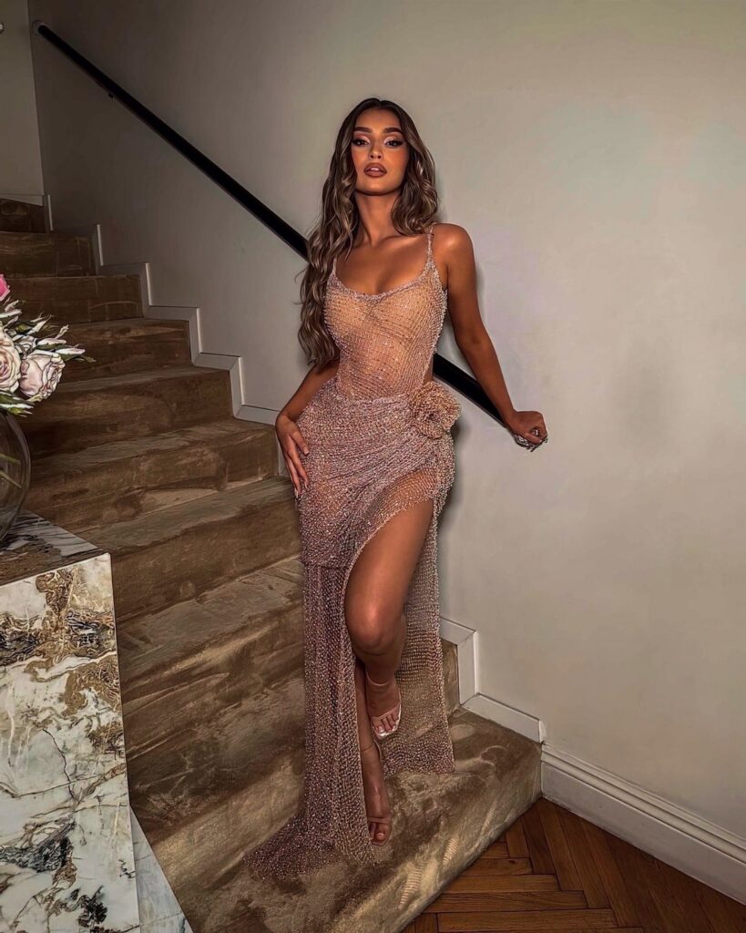 A woman in a sparkling rose gold sequined gown posing on a carpeted staircase.