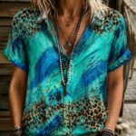 A person wearing a teal tie-dye shirt with leopard print patterns and layered necklaces.