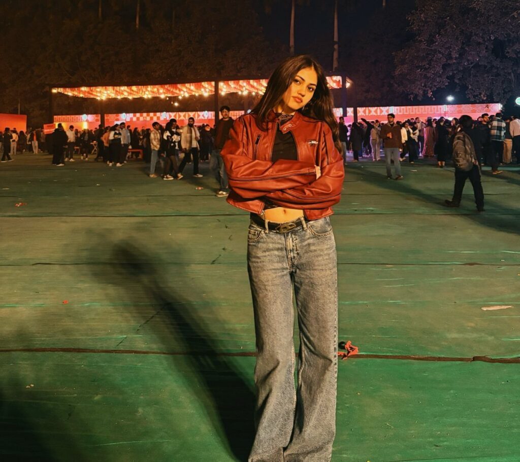 Woman posing in a red leather jacket and blue denim jeans at an outdoor night event.