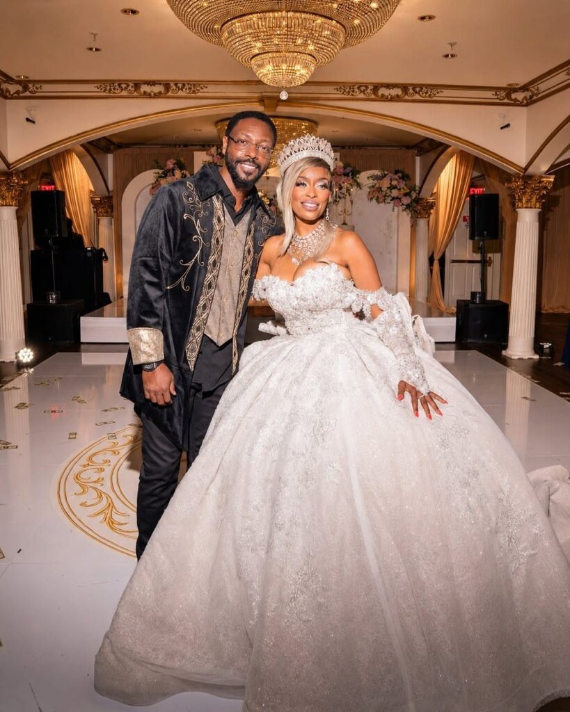 A man in black and gold attire and a woman in a white ball gown posing in a ballroom.