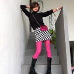 A person posing on stairs wearing a checkered skirt and bright pink leggings with black boots.
