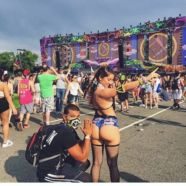 A woman in colorful booty shorts poses for a photo at an outdoor music festival.