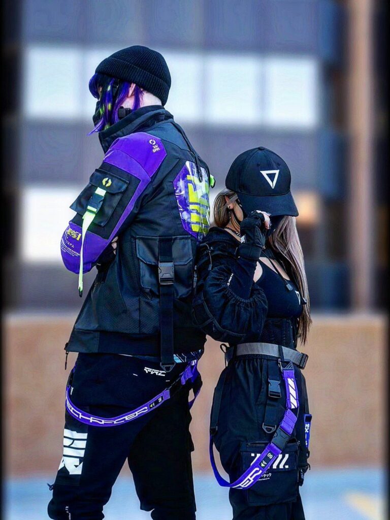 Two people posing in black and purple streetwear outfits against a blurred urban background.