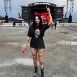 A woman in a black graphic t-shirt, fishnet tights, and combat boots posing at a music festival.