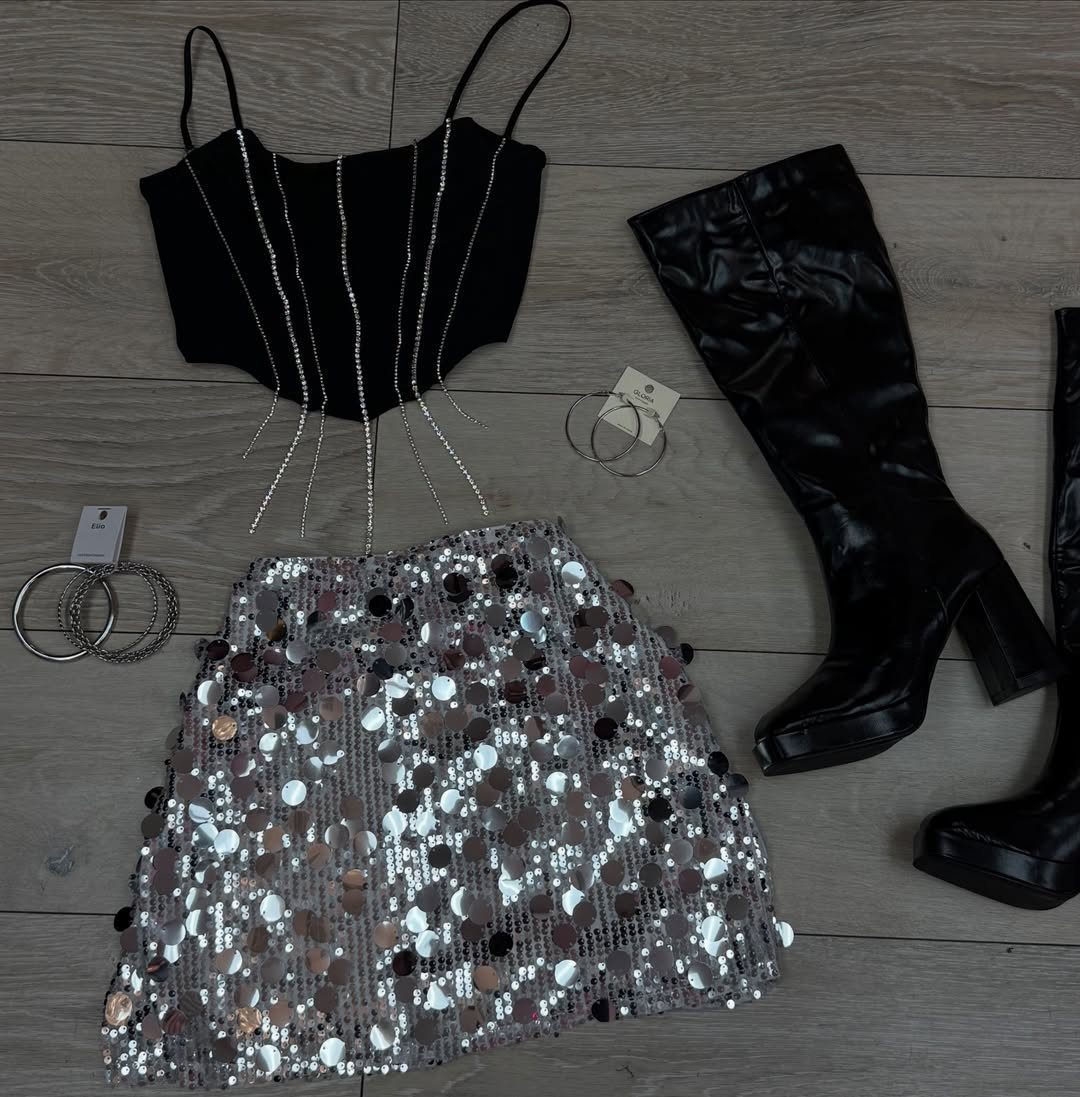 Black corset top, silver sequined skirt, and black boots laid out on a wooden floor.
