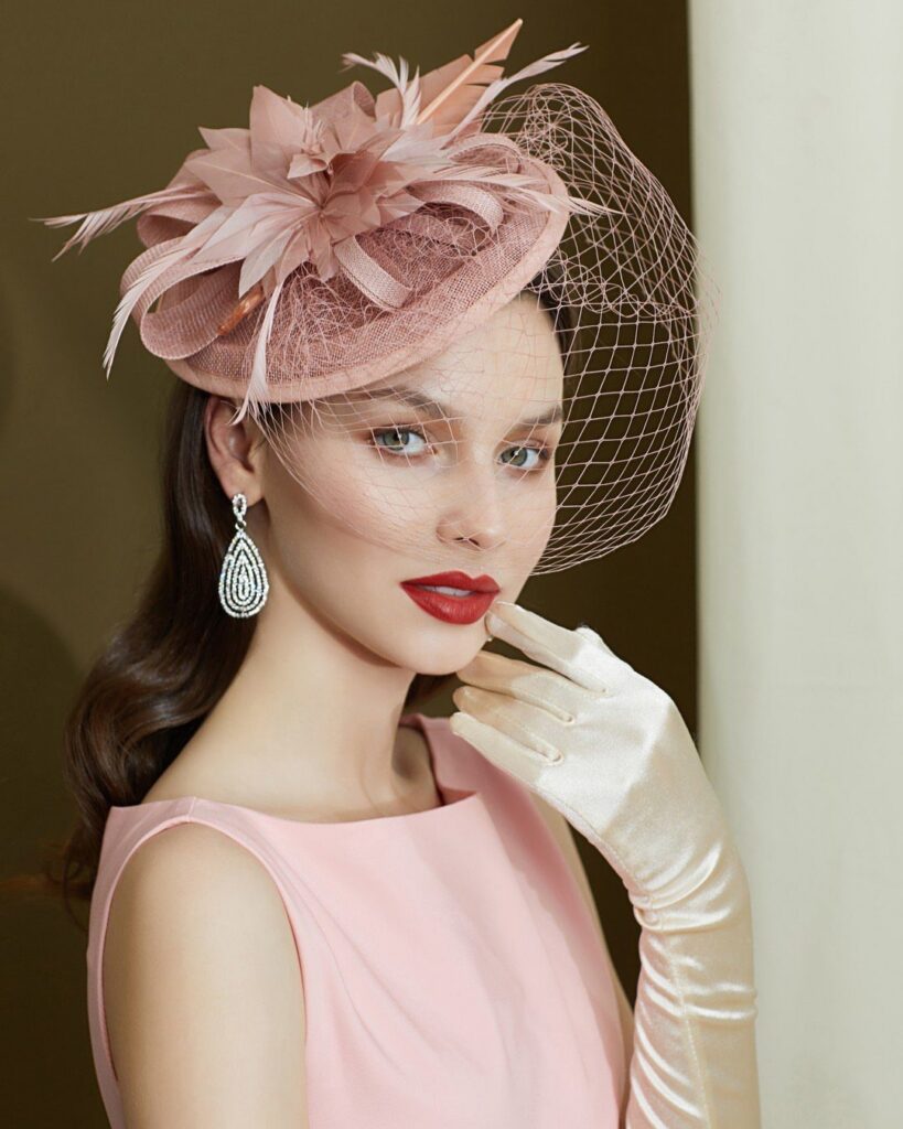 Woman wearing an elegant pink fascinator hat with feathers and a mesh veil.