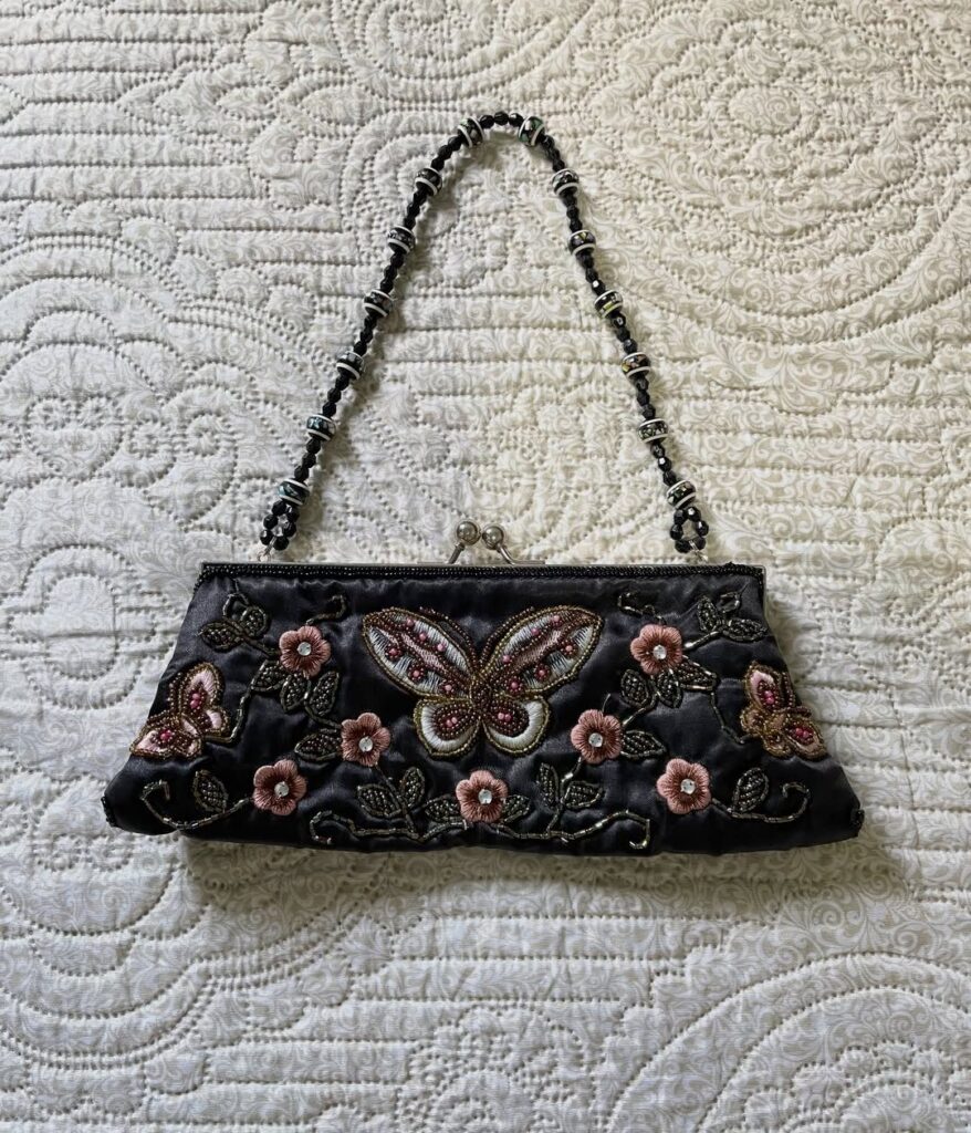 Embroidered black satin clutch bag with butterfly and floral patterns on white quilted fabric.