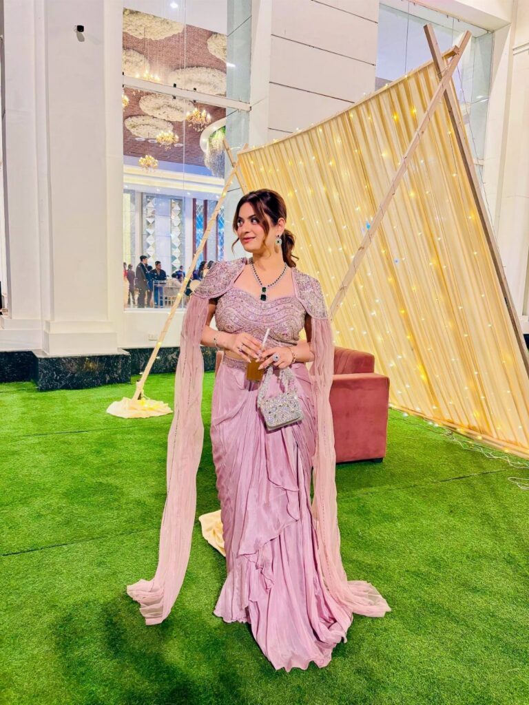 Woman in an embellished lavender saree posing on green grass near a decorative tent.